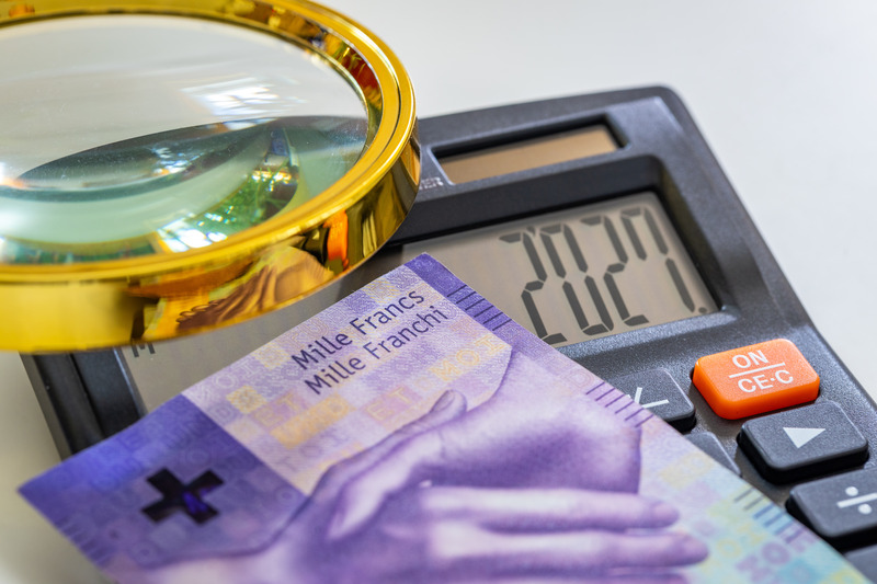 A thousand Swiss franc note resting on a calculator next to a magnifying glass.