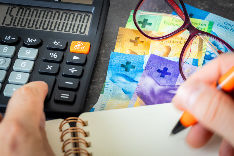 Calculator and reading glasses resting on Swiss franc banknotes, illustrating multi-currency retirement planning and dollar inflation hedging for U.S. investors.